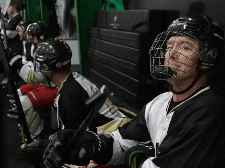 Adult hockey players sitting on the bench during a game at an indoor hockey rink.