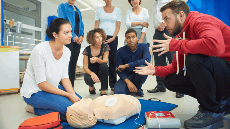 CPR training class where an instructor demonstrates chest compressions and AED use on a CPR mannequin