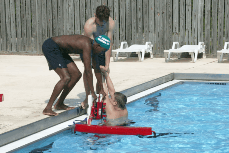 Lifeguards assisting a swimmer during a poolside rescue at a public swimming pool, demonstrating water safety and emergency response.