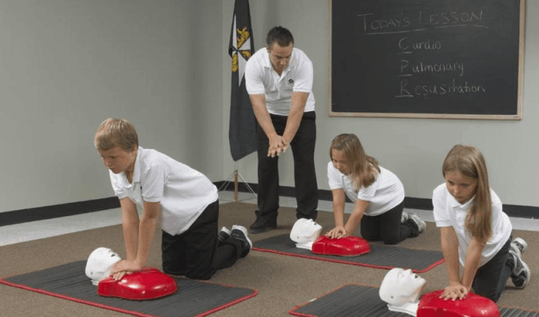 Children learning hands-only CPR chest compressions under instructor guidance during a CPR training class.