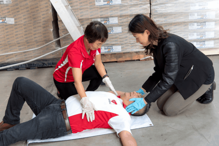 Co-workers providing CPR to an unconscious man during a workplace emergency before paramedics arrive