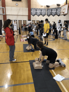 Students practice CPR on training mannequins during a school emergency response and first aid awareness event.