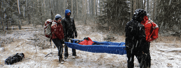 Wilderness first aid responders carry injured hiker on improvised stretcher after emergency in remote forest