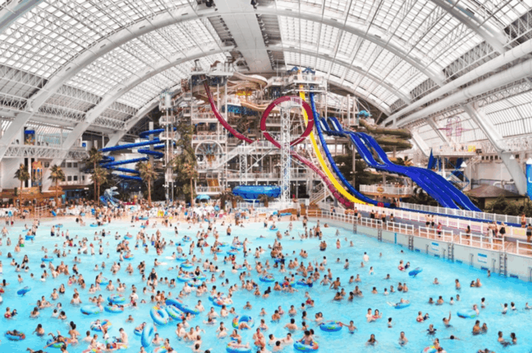 Busy indoor water park with families swimming as lifeguards monitor safety at a large public pool facility.