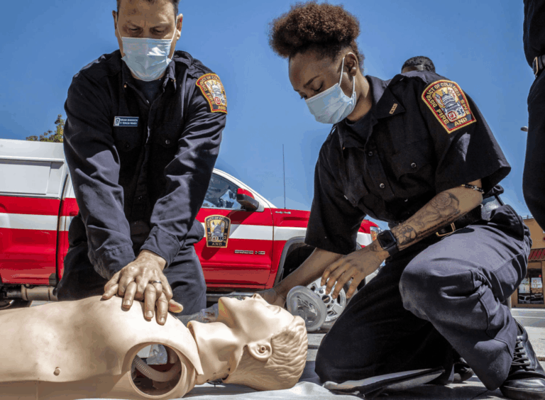 Firefighters practising CPR and rescue breathing on a training mannequin during an outdoor emergency response drill