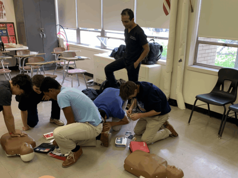 Students practicing CPR and AED use during a hands-on first aid training session in a classroom setting.