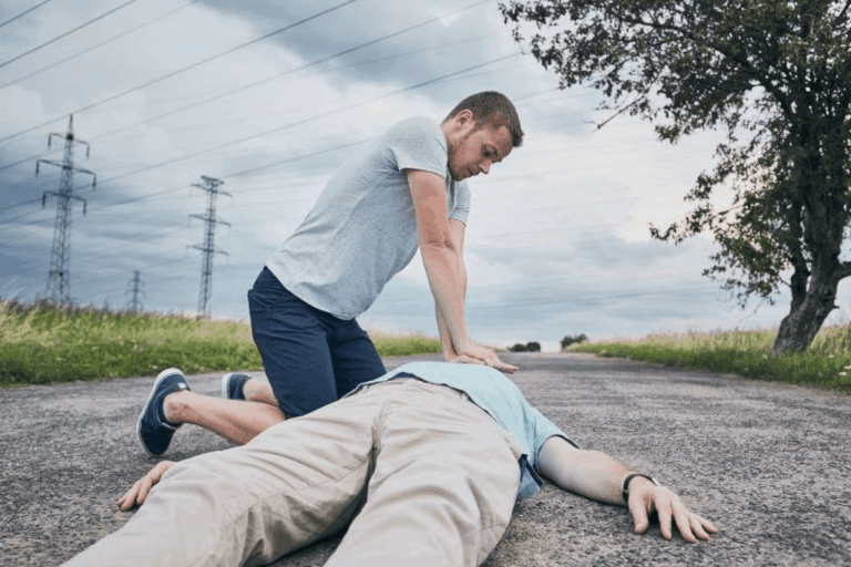 Bystander performing CPR on an unconscious person after sudden cardiac arrest on a roadside