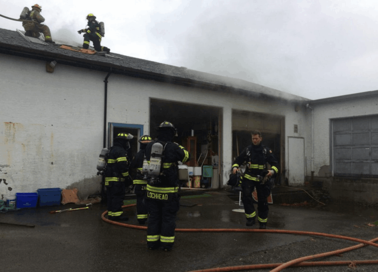 Firefighters responding to antique store fire in Qualicum Beach, conducting roof ventilation and rescue operations amid heavy smoke.