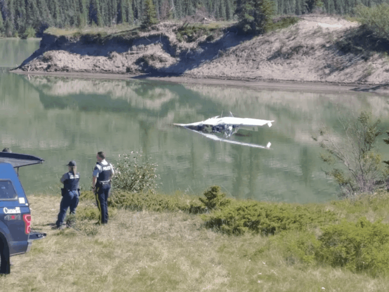 Small aircraft partially submerged in the Athabasca River near Jasper as police officers observe the crash scene.