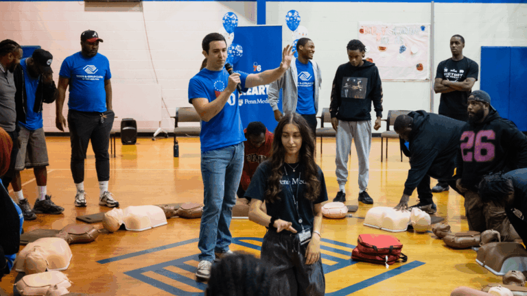 Bystanders practicing CPR and AED training during a community lifesaving demonstration inside a gymnasium.